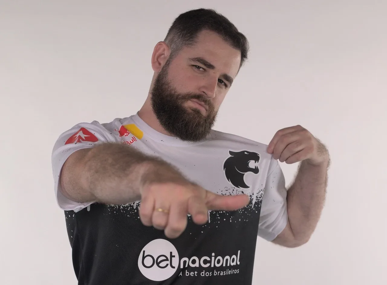 FalleN com a camisa branca e preta da FURIA, apontando para a câmera e segurando o escudo da pantera